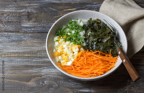 Fresh seaweed salad with shredded carrots, chopped eggs and onions in ceramic bowl on rustic wooden table