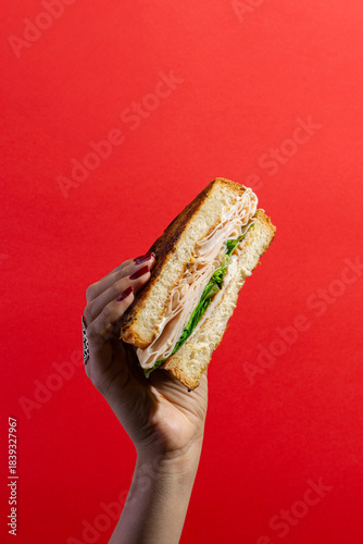Sándwich de jamón y queso levantado con la mano sobre fondo rojo