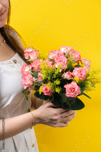 Mujer sosteniendo ramo de rosas rosadas sobre fondo amarillo