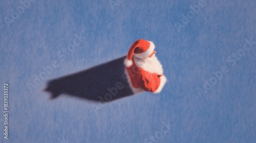 Christmas Santa hat (red and white trim) attached to flying dark cloth, set against soft blue textured background. Festive holiday whimsical creative scene, seasonal decor ideal for wallpaper, poster