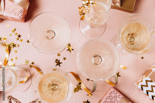 Festive Christmas new year 2026 background celebration scene featuring elegant champagne glasses, colorful gift boxes, and shimmering confetti on a soft pink background