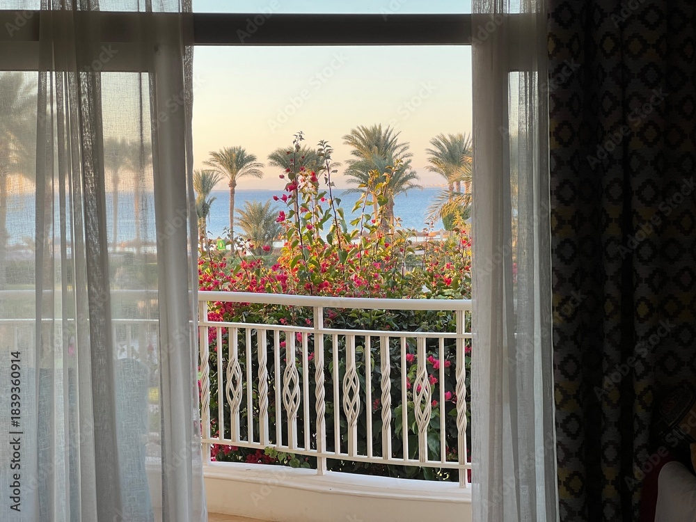 Fototapeta premium View from the room onto the balcony and the turquoise sea with the resort's palm trees at sunset. Travel destinations. Summer vacations. Year-round vacations