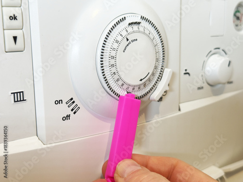 Closeup of a man’s hand selecting a segment of tabs on a manual programmer, to set the activation period for a domestic gas boiler for heating and hot water.