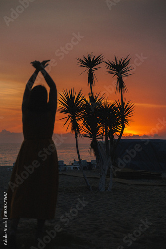 Silhouette Dancer Beach Sunset Palms Backlit, Graceful Arms Raised Against Orange Sky, Calm Ocean Horizon,