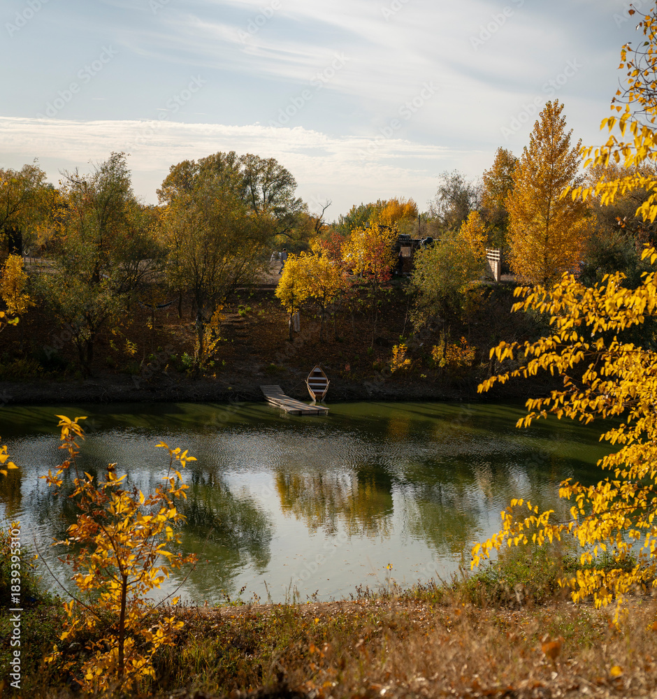 Fototapeta premium A person rows a small boat on a lake surrounded by trees in autumn colors