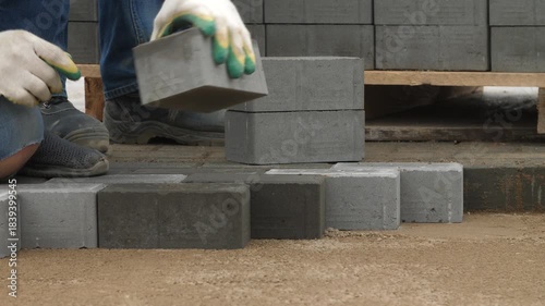 Construction worker man laying concrete paving stones on sand outdoors.