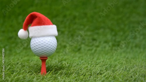 A golf ball wearing a Santa hat on green grass.