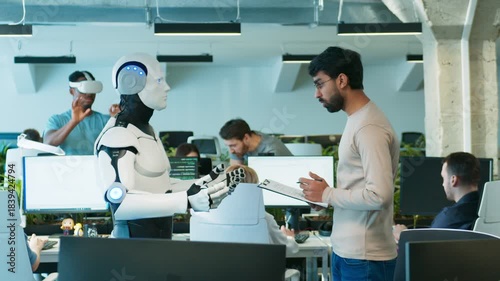 Male engineer checking robot functions. Bearded man reviewing clipboard while giving instructions. Humanoid standing still awaiting command. Raising hands. Tech office with active staff.
