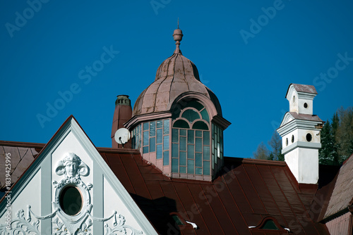 House roof with brick chimney stack and attached historic gable turret against a blue sky in Mariazell, Austria;