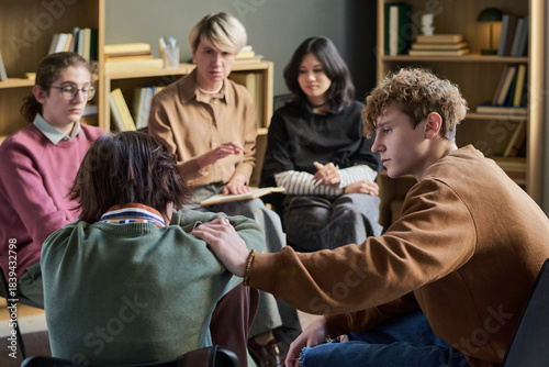 Group of diverse young people and teenagers sitting in circle participating in group therapy session, young man comforting distressed teenager, multiethnic people listening