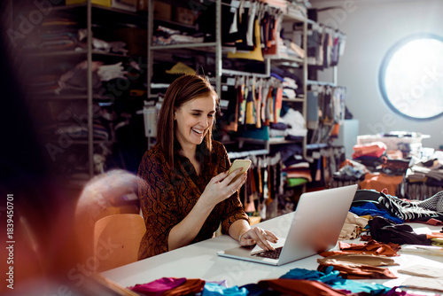 Adult woman laughing, managing online shop in fashion studio