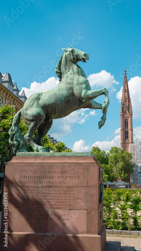Bronze horse sculpture in Wiesbaden on a clear spring day, with church spires and blue skies dotted with white clouds in the background.