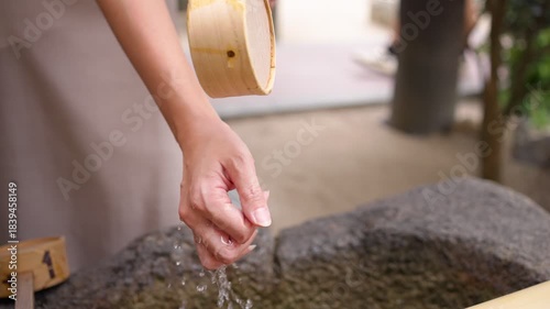 Slow motion of woman washing her hands with water from a bamboo dipper at a stone basin in a Japanese temple. A traditional act of ritual purification before entering.