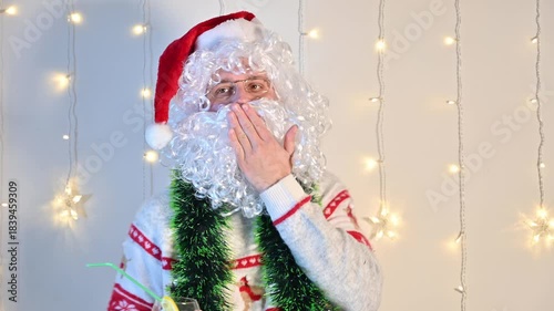 A man dressed as Santa Claus on a white background with festive lights, blowing air kisses, creating a warm, playful, and charming holiday scene.