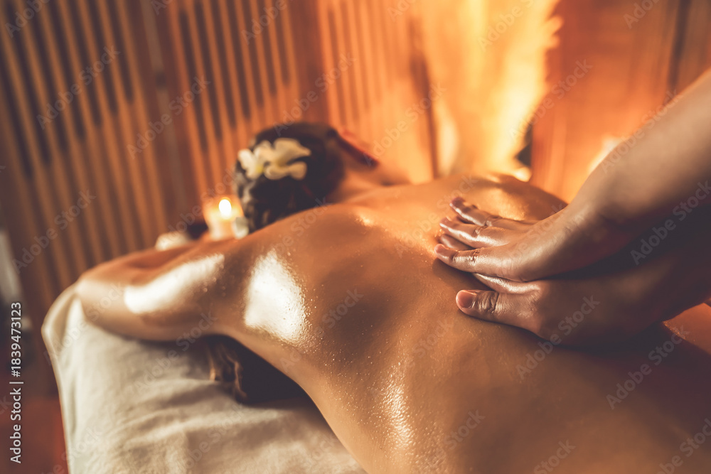 Naklejka premium Caucasian woman customer enjoying relaxing anti-stress spa massage and pampering with beauty skin recreation leisure in warm candle lighting ambient salon spa at luxury resort or hotel. Quiescent