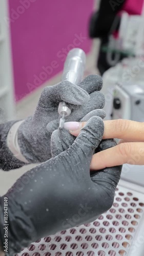 Beautician shaping client nail with electric file in salon