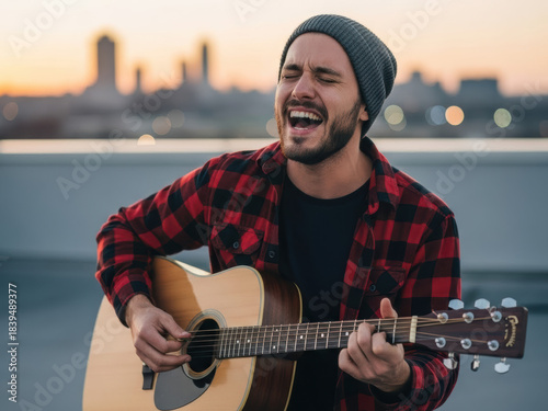 Man singing and playing acoustic guitar on a rooftop at sunset