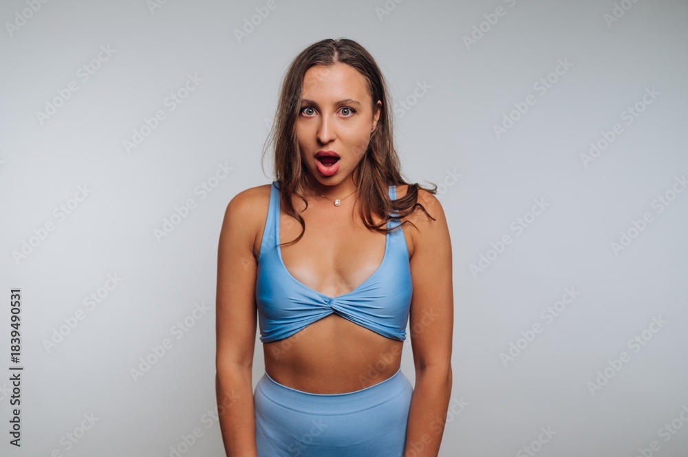 Fototapeta premium Woman in blue sportswear with surprised expression against gray background.