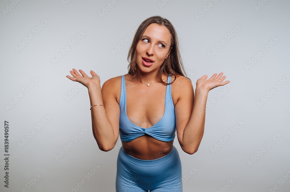 Fototapeta premium Woman in blue activewear shrugging with a playful expression.