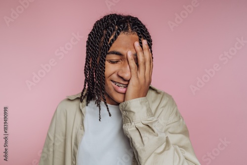 Smiling young person with braided hair covering face, pink background.