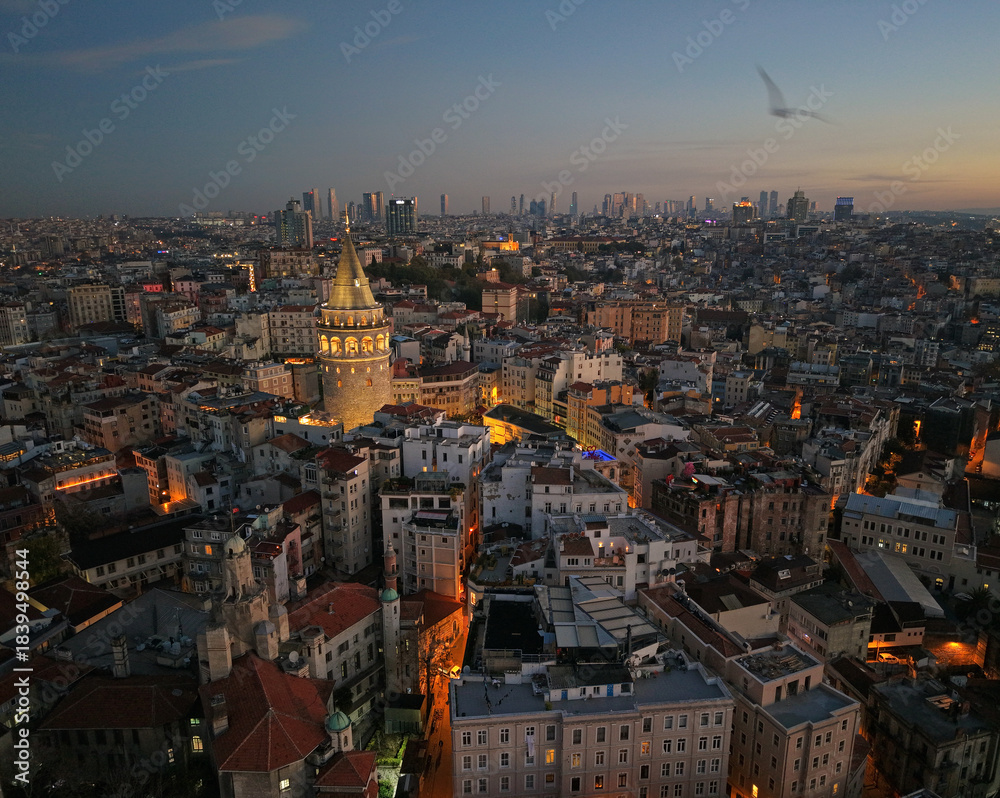 Naklejka premium Morning view of Galata Tower and cityscape in Istanbul with lights illuminating streets and buildings at sunrise. Flying around iconic Galata Tower in historic Beyoglu district 