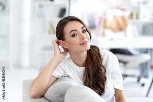 Woman in a white shirt is sitting on a gray couch, smiling