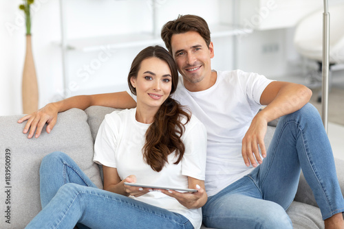 Man and woman are sitting on a gray couch, smiling at each other.