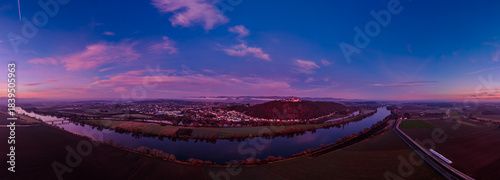 Sonnenuntergang über der Stadt am Fluss mit Bergen im Hintergrund