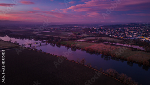 Blick auf die Landschaft bei Sonnenuntergang über einem Fluss und der Stadt im Hintergrund
