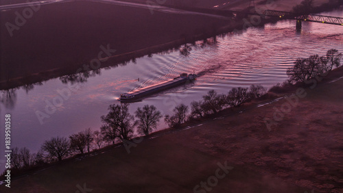 Ein Schiff fährt auf dem Fluss bei Sonnenuntergang in einer ländlichen Umgebung mit Bäumen am Ufer