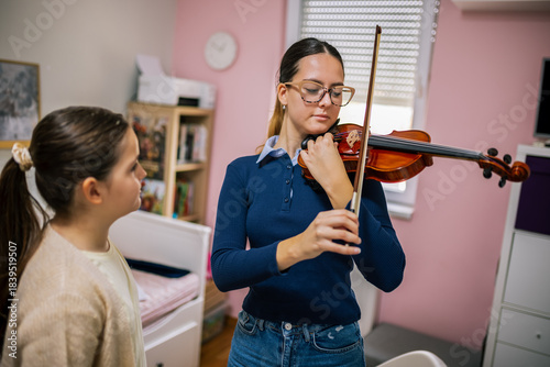 The instructor shows the girl how to hold the violin and move the bow correctly during an at-home music lesson.