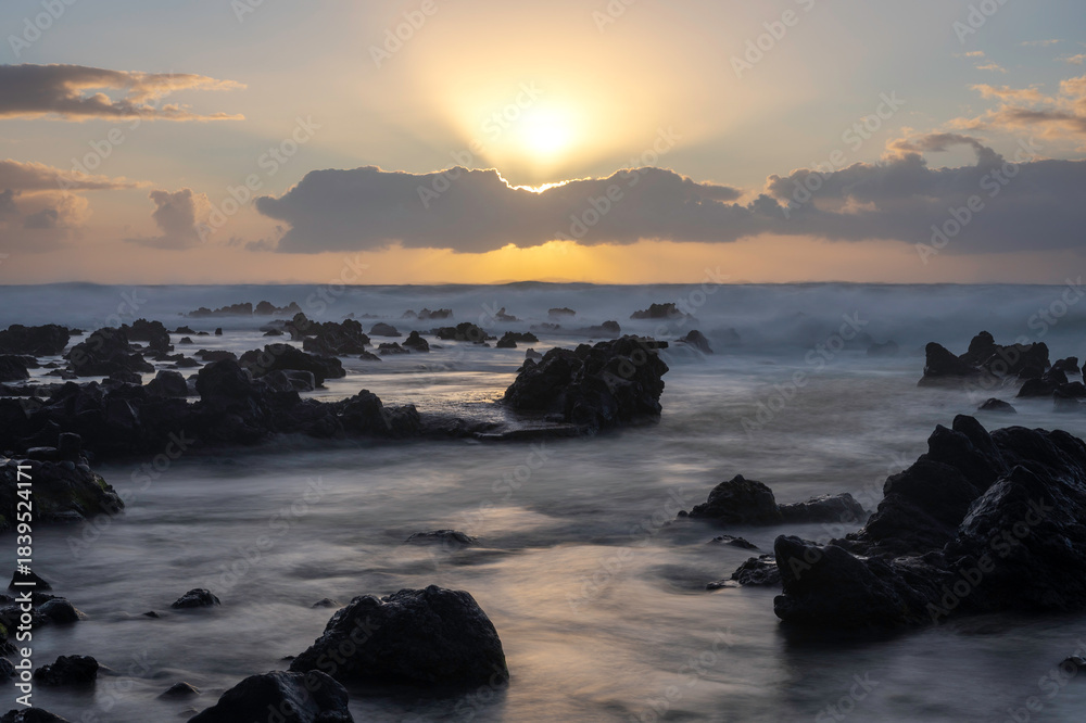 Obraz premium Panoramic image of a sunset in the Azores showing the sun setting over the sea, with large rocks emerging from the water