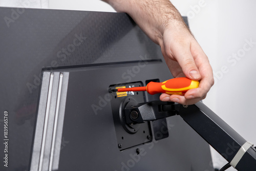 Fotografia Person's hand uses a precision screwdriver to securely fasten a monitor arm onto
