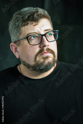 Portrait of young Caucasian man with glasses, beard on black.