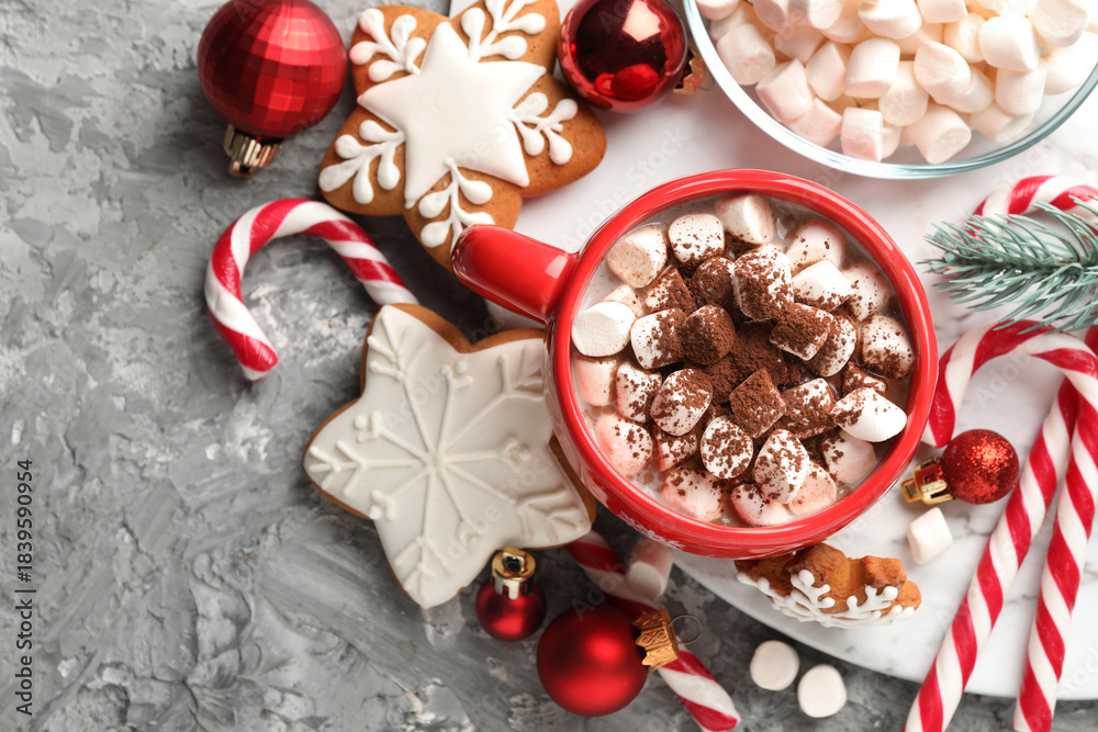 Obraz premium Tasty cocoa with marshmallows, candy canes, gingerbread cookies and Christmas decor on grey table, flat lay. Space for text
