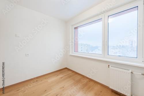 Bright Empty Room With Wooden Flooring and Large Window Overlooking Urban Scenery