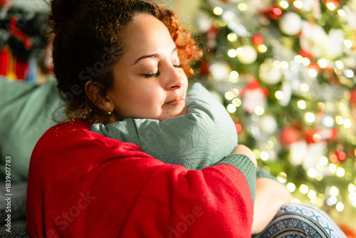 Woman finding comfort, hugging pillow near christmas tree