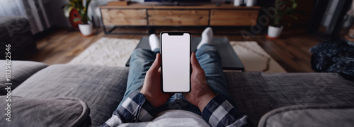 Cozy Leisure: A person relaxes on a comfortable sofa, holding a smartphone with a blank screen, offering a glimpse into the everyday simplicity of digital life and modern relaxation.