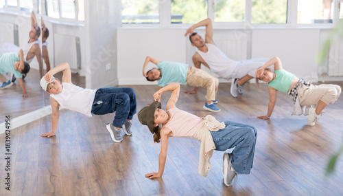 Sports girl performing breakdance moves. Group of teenagers dancing and enjoying hip-hop in modern sports room