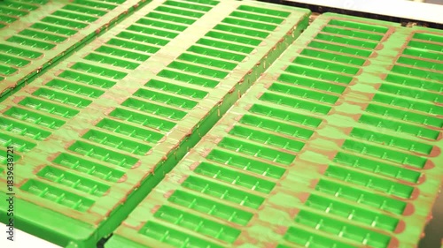 Green empty molds for chocolate bars move along a conveyor belt towards a filling machine in a modern food production factory, demonstrating the automated process.