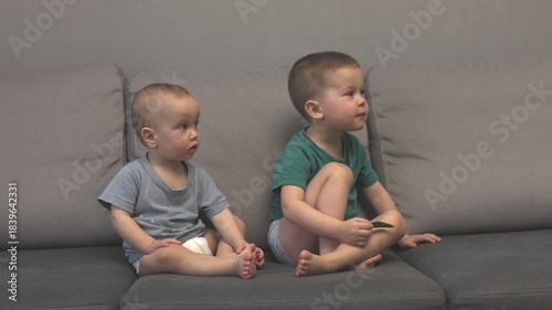 Young siblings enjoy screen time, showing curiosity and innocence while relaxing together on the cozy couch