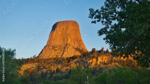A view of Devil's Tower in the golden light of the morning sunrise and a clear blue sky.