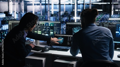 Data center system administrators use PC to monitor neural network using AI LLM. Asian man and colleague at work using artificial intelligence to oversee servers powering machine learning, camera A