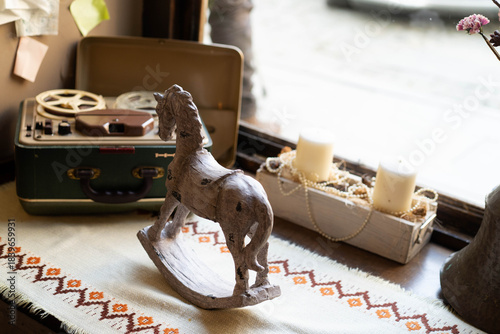 A vintage rocking horse stands proudly beside a green travel case adorned with film reels. Candles flicker softly on a woven table runner, creating a warm and inviting atmosphere.
