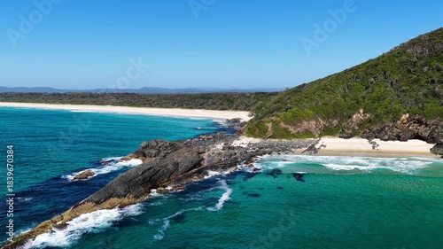Aerial video capturing gentle ocean waves rolling onto the wide sandy shoreline at Janies Corner, Seven Mile Beach in Forster