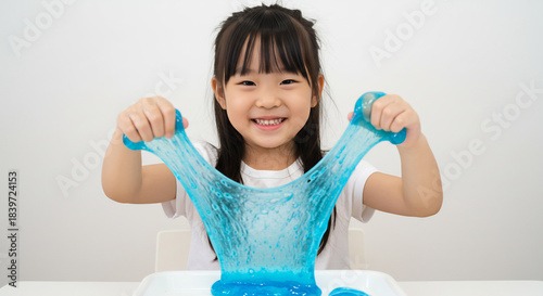 Smiling young child enthusiastically stretches bright blue slime illuminated by soft natural light for a playful moment. AI Generated