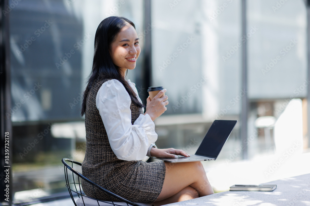 Fototapeta premium Asian young oman using laptop while holding reusable coffee. 