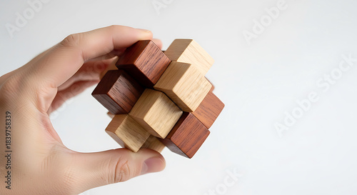 Hand holding interlocking wooden cube puzzle with light and dark wood image