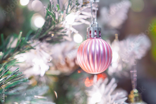 Close-up of shiny pink Christmas ball hanging on Christmas tree with Christmas light background