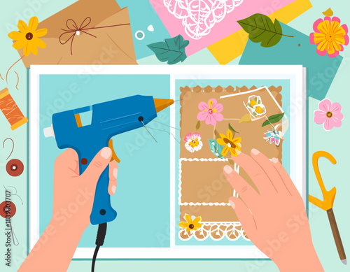 Hands use a hot glue gun to create a beautiful scrapbook page with flowers and butterflies. A creative, top-down view of a DIY crafting project.